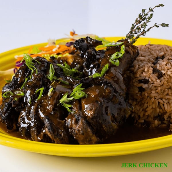 Jerk chicken with rice and peas, garnished with scallions and thyme, on a yellow plate.