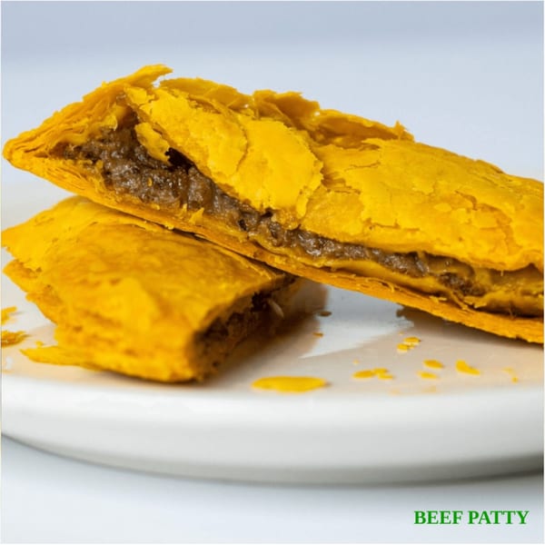 Two Jamaican beef patties, one split open to reveal the savory filling, on a white plate.